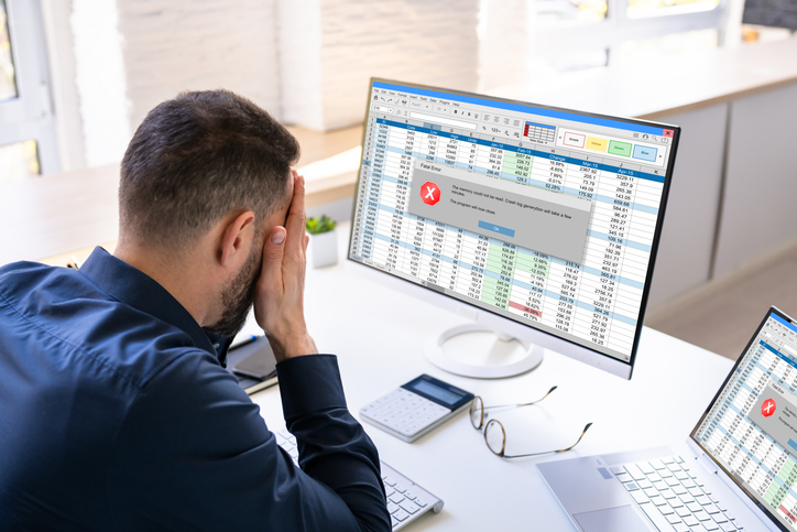 A man with his head in his hands in front of a spreadsheet showing an error